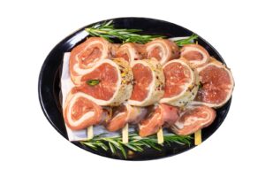 Raw Lamb Pinwheels on Skewers With Herbs on Black Plate